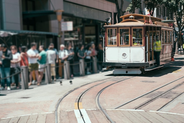 日当たりの良い街の通りでケーブルカーに乗るのを待つために並んでいる観光客のぼやけたビューの長い列。カリフォルニア州サンフランシスコの有名な路面電車。公共交通機関の概念を表す通勤者