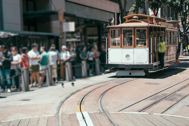 Blurred view long queue of tourists lining up to wait to board
cable car on sunny city street. famous tramway in san francisco
california. commuter standing for public transport concept