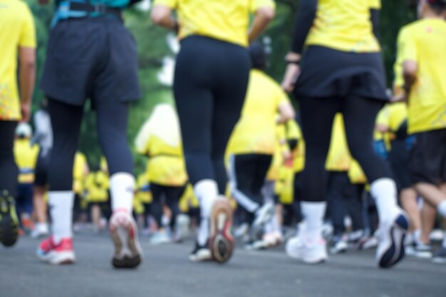 Photo blurred view rear view of many runners wearing yellow shirt running on asphalt during marathon race