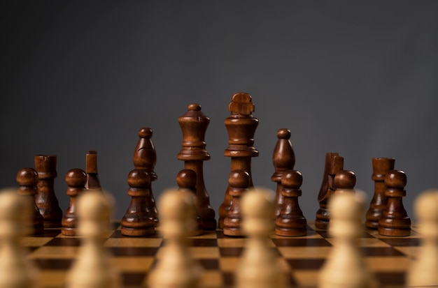 Blurred white pawns against group of black chess figures on chessboard