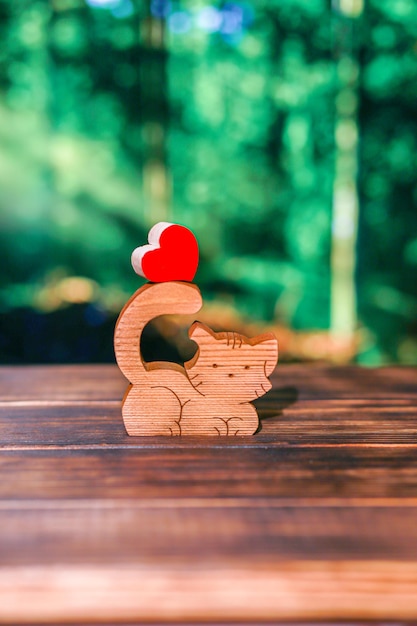 Blurred wooden puzzle in the form of a handmade cat with a heart on the background of a blurry forest