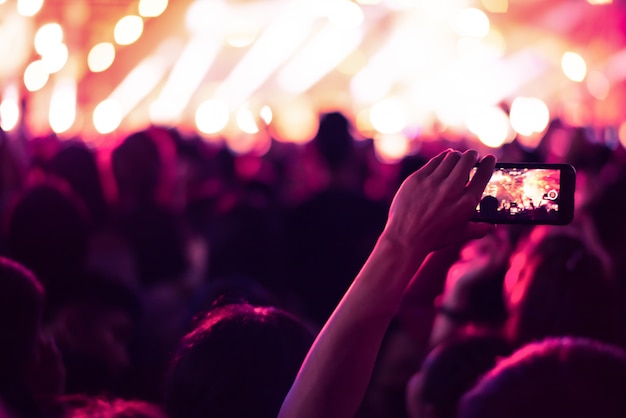 スマートフォンを持っている手のぼんやりしたカラフルな背景は、写真の人々がコンサートで混雑している。