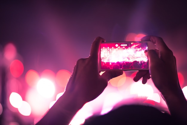 blurry colorful background of hand holding smart phone to taking photo people crowded in concert.