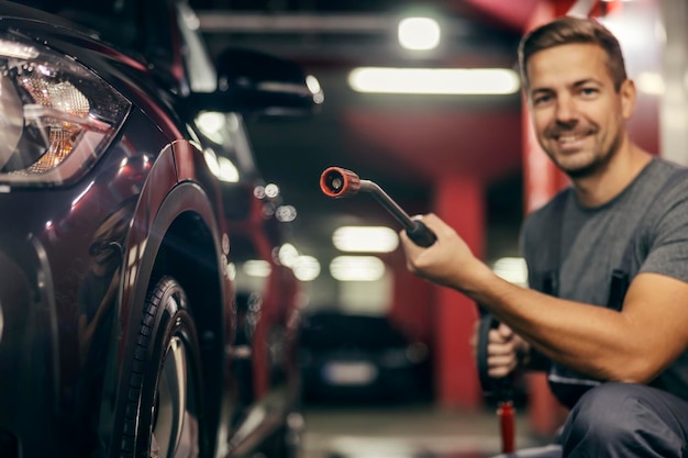 Blurry image of a car wash station worker holding a water gun next to a car