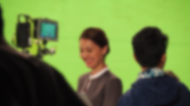 Blurry images of making tv commercial movie video in big green\
screen background. film crew team working with actor. recording by\
professional digital camera and lighting set. film behind the\
scenes