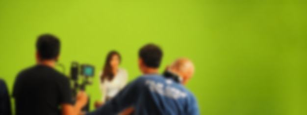 Blurry images of making tv commercial movie video in big green\
screen background. film crew team working with actor. recording by\
professional digital camera and lighting set. film behind the\
scenes