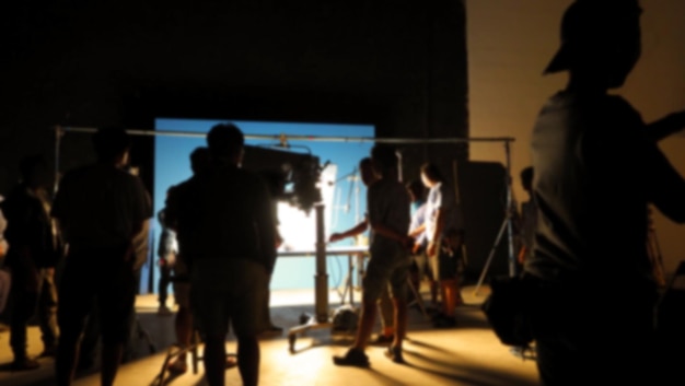 Blurry images of making video production shooting studio in silhouette which have professional equipment such as camera tripod and blue screen backdrop set for chroma key technique in post process