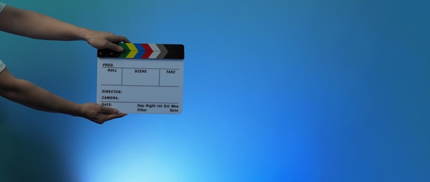 Размытые изображения грифельной доски или доски с хлопушкой. Рука держит пустую пленочную доску на цветном фоне в студии для съемок или записи фильмов. Планшет для видеопроизводства Youtuber.