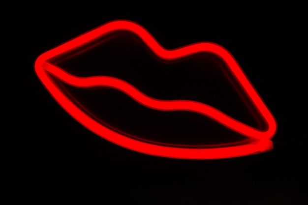 Foto primo piano sfocato delle labbra rosse al neon su uno sfondo nero isolato.