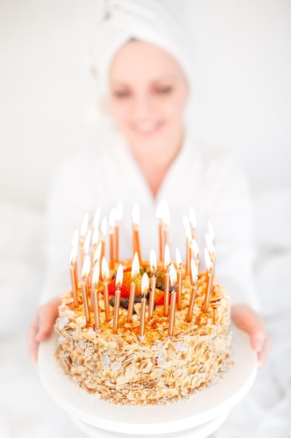 A blurry portrait of a girl in a bath towel and bathrobe with a birthday cake close  up with candles Birthday celebration early in the morning After the shower