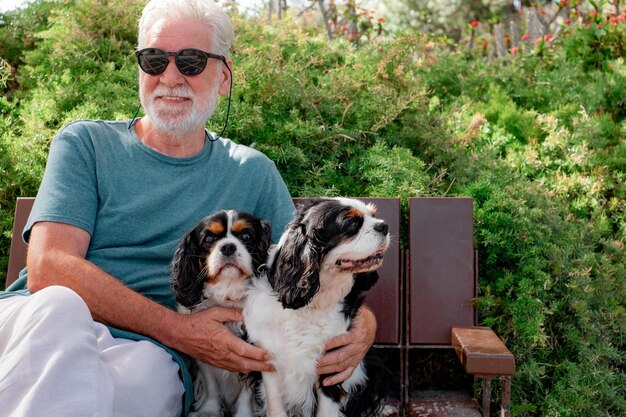 Blurry Senior smiling man in black sunglasses sitting in the park with his two cavalier king dogs