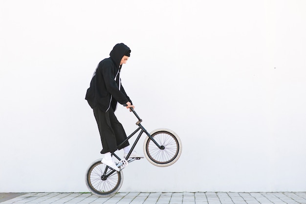 Bmx racer makes a trick in on white wall. Bmx rider with a bicycle in flight on white