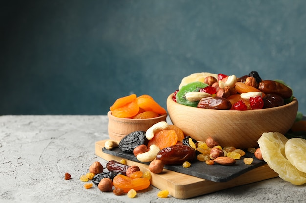 Board and bowls with dried fruits and nuts on gray table