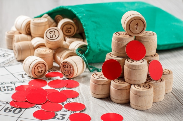 Board game lotto. Stacked wooden lotto barrels with bag, game cards and red chips for a game in lotto on gray background