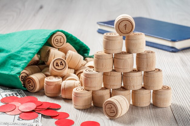 Board game lotto. Stacked wooden lotto barrels with bag, game cards and red chips for a game in lotto and notebook on the background