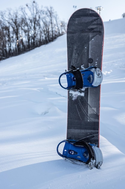 Board for snowboarding in the snow on the background of a ski slope vertical photo The concept of snowboarding a winter sport