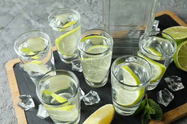 Photo board with bottle and shots of vodka with lime on gray surface