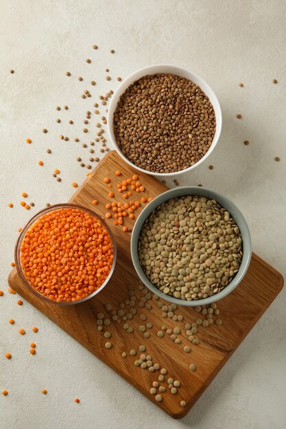 Board with bowls with legumes on white surface