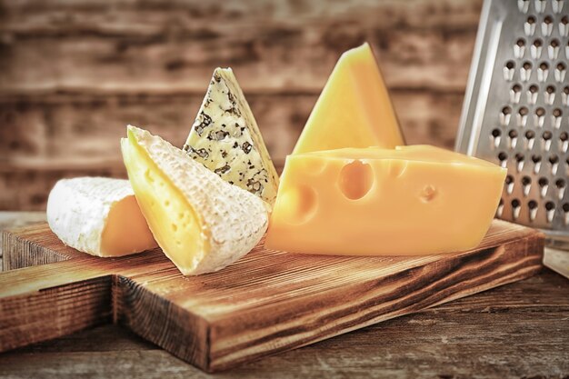 Board with cheese and grater on wooden background