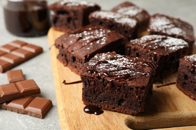 Board with chocolate cake slices and chocolate on grey background, close up