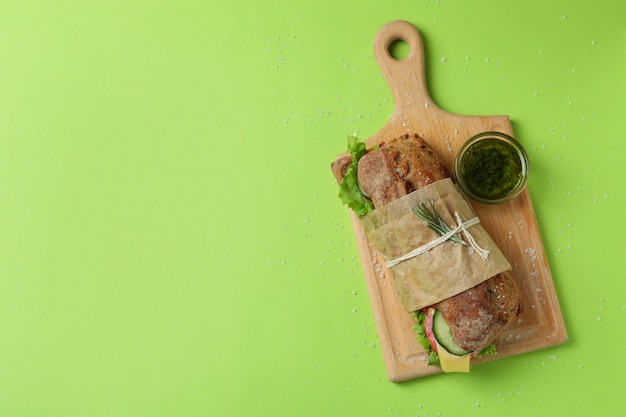 Board with ciabatta sandwich, sauce and salt on green background