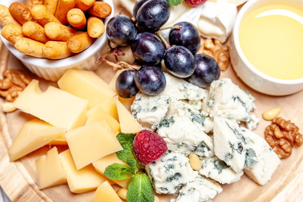 Board with different types of cheese. Cheese mix set dor blu chedar parmesan brie honey sauce finger bread and grape on wooden palte. Restaurant menu breakfast plate. Healthy snack assortment.