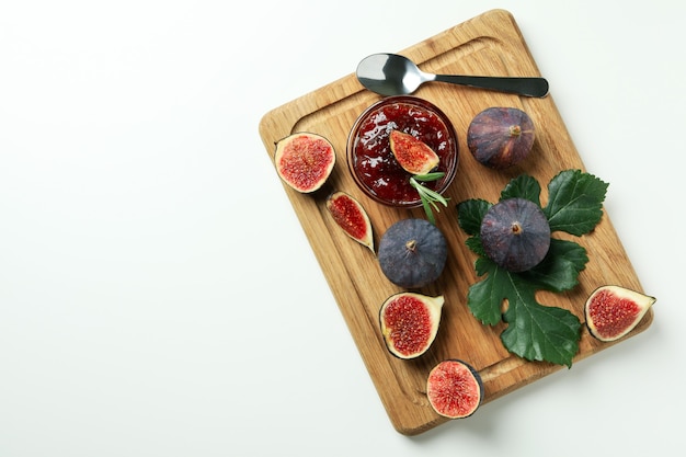 Board with fig jam, ingredients and spoon on white background