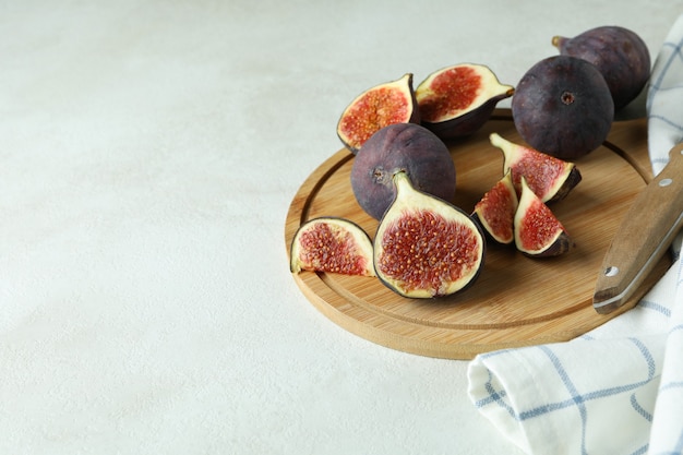 Photo board with fig, knife and kitchen towel on white textured table