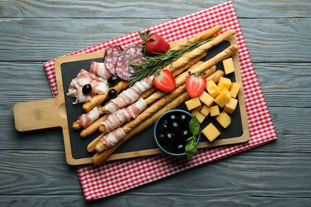 Board with grissini and snacks on wooden surface