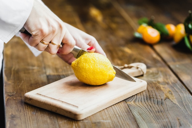 Board with lemon. cook cutting a lemon, holding a kitchen knife in her hand, cutting a lime