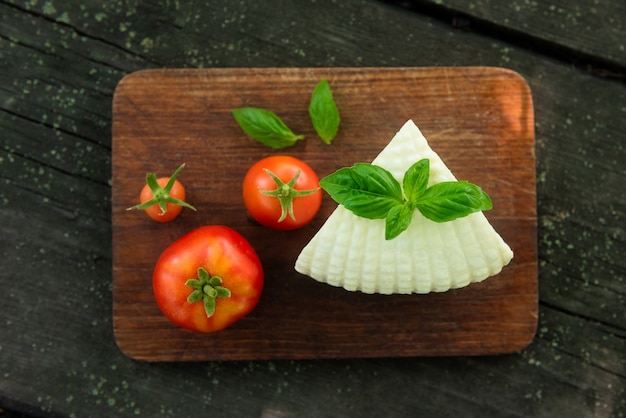 Photo board with mozzarella cheese, tomato and basil on dark background. top view