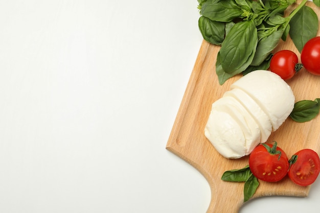 Board with mozzarella cheese, tomato and basil on white background