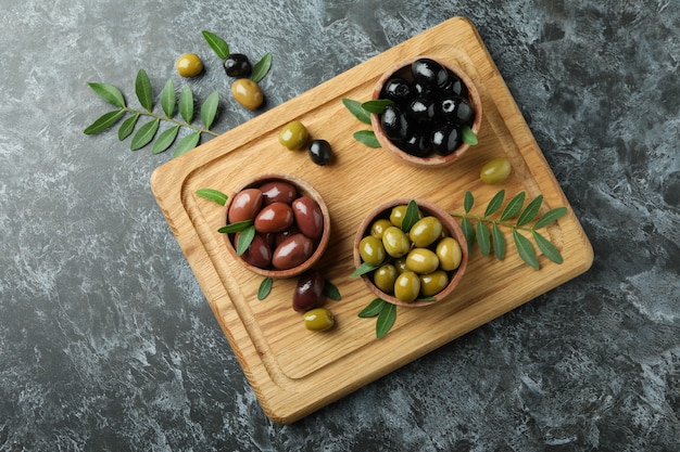 Board with olives and leaves on black smokey background