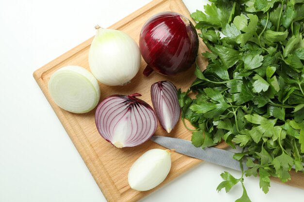 Tagliere con cipolla, prezzemolo e coltello su sfondo bianco