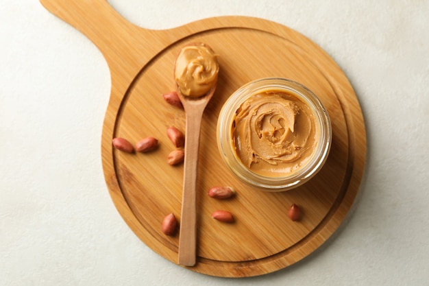 Board with peanut, spoon and jar with peanut butter on white background