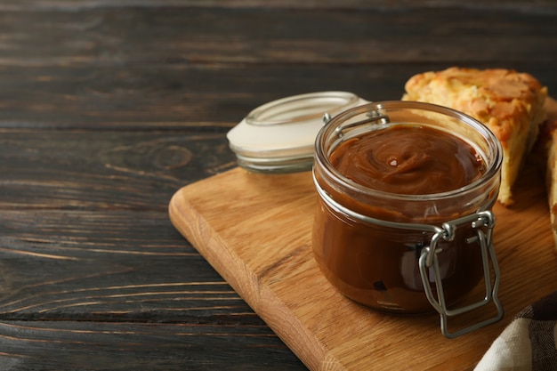 Board with pie and caramel condensed milk on wooden surface