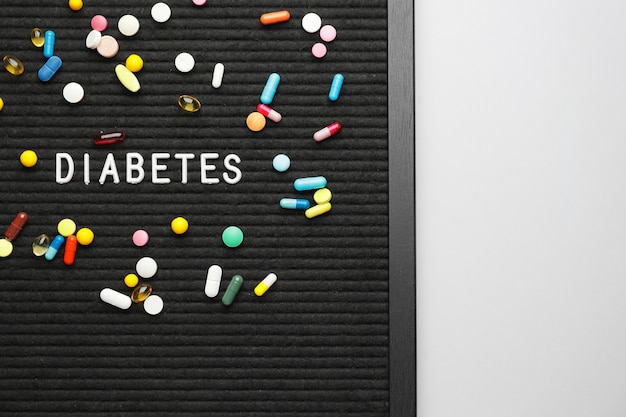 Board with pills and word DIABETES on white
