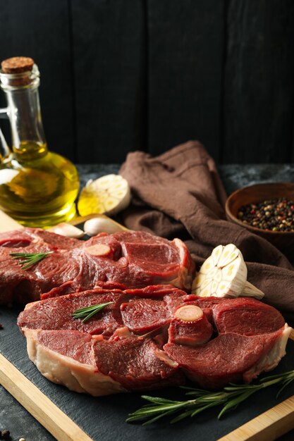 Board with raw steak meat, herbs and spices on black smokey