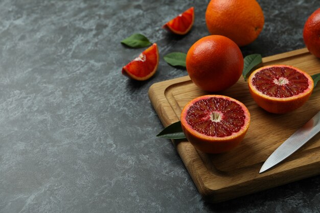 Photo board with red oranges, leaves and knife on black smoky table