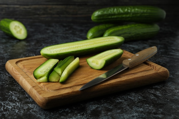 Board with ripe cucumber and knife on black smokey table