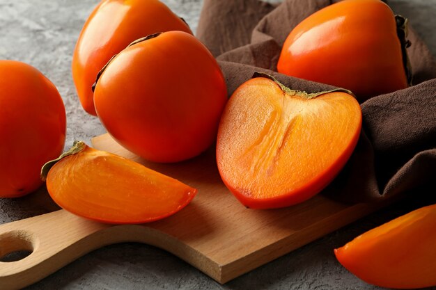 Board with ripe persimmon and kitchen towel on gray background