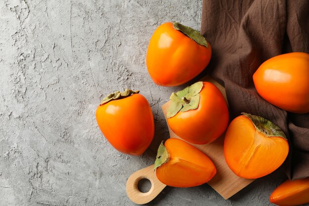 Board with ripe persimmon and kitchen towel on gray background