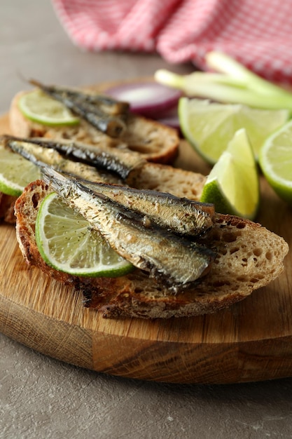 Board with sandwiches with sprats on gray textured background