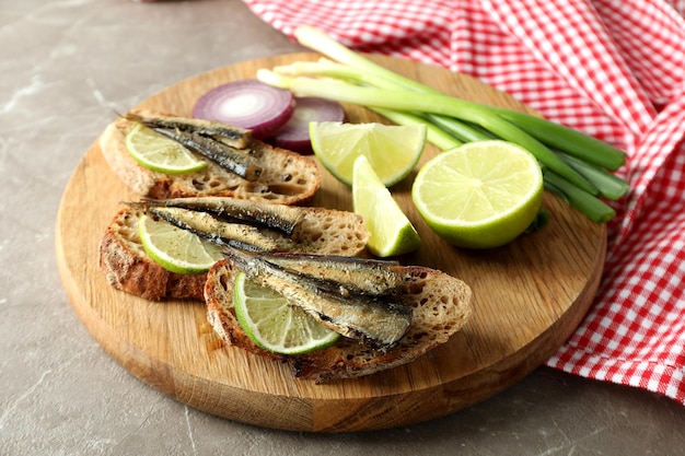 Board with sandwiches with sprats on gray textured background