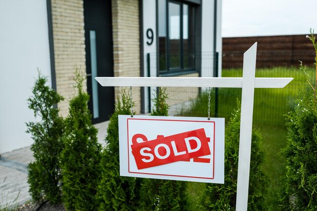 Board with sold lettering near green trees and new house