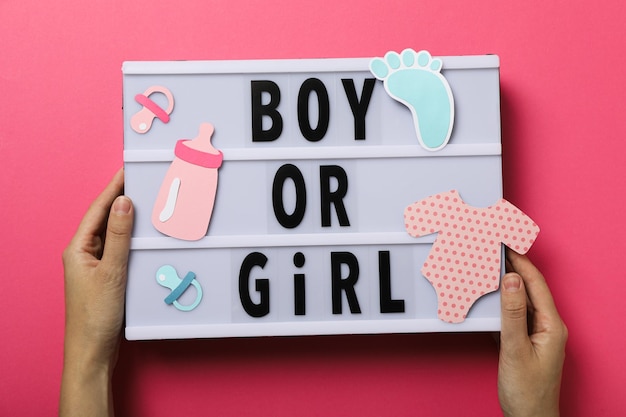 Photo board with text in female hands and paper baby things on pink background top view