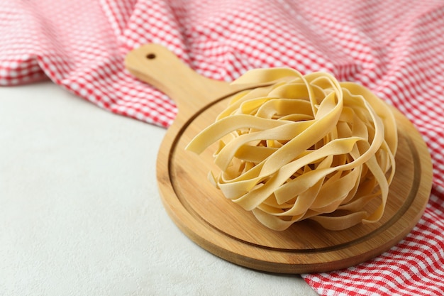 Board with uncooked pasta and kitchen towel on white textured