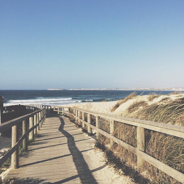 Boardwalk leading towards sea against blue sky