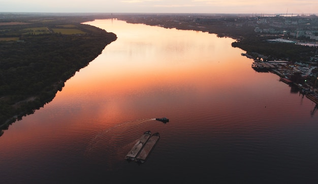 Boat and barge with sand sails along the coast along the wide  river on the sunset. aerial view