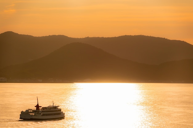 ボートフェリーは日本の高松島に沿って旅行し、休暇と日本の旅行コンセプトのための黄金の夕日の反射空